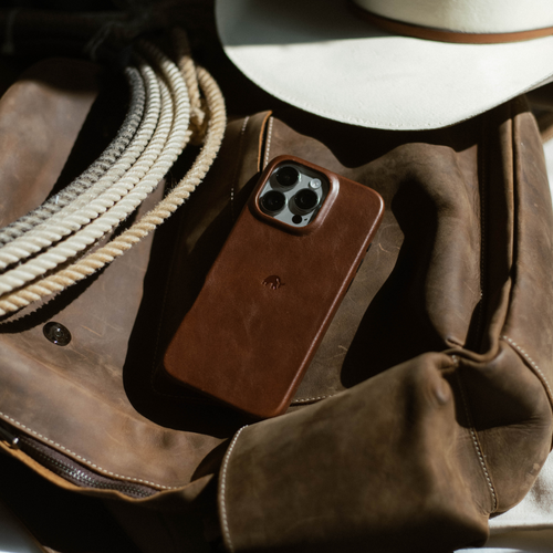 Terra minimalist brown leather phone case resting on a worn leather bag beside coiled rope and a white hat