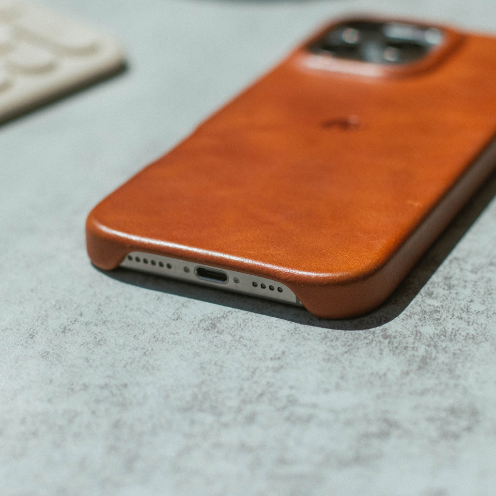Sienna leather phone case on a table showing bottom charging port and camera cutout.