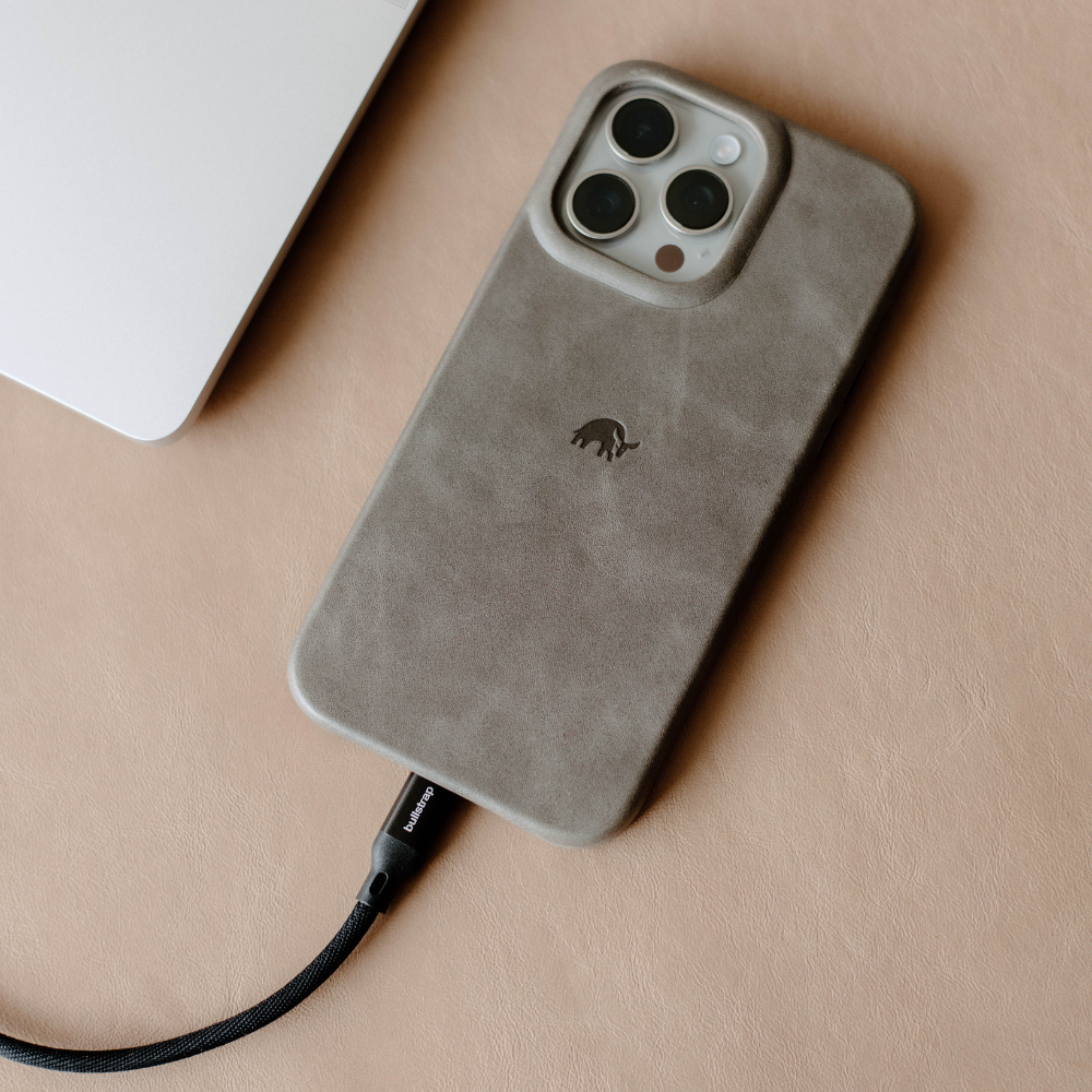 Taupe suede phone case with small elephant logo, charging cable labeled bullstrap plugged into the bottom.