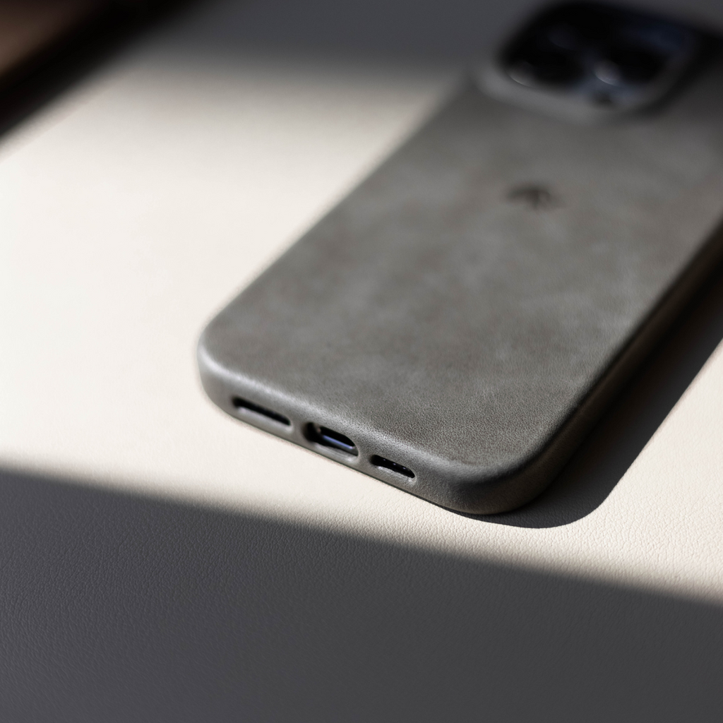 Slate-gray leather iPhone case face-down showing rounded corner and bottom speaker and Lightning port cutouts in soft light