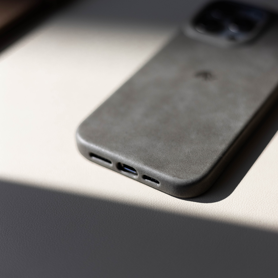 Slate-gray leather iPhone case face-down showing rounded corner and bottom speaker and Lightning port cutouts in soft light