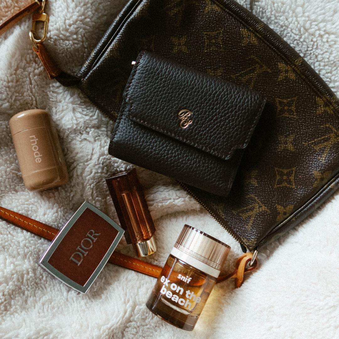 Dark leather trifold wallet on monogram pouch with cosmetics labeled rhode, DIOR, and a snif bottle reading ex on the beach