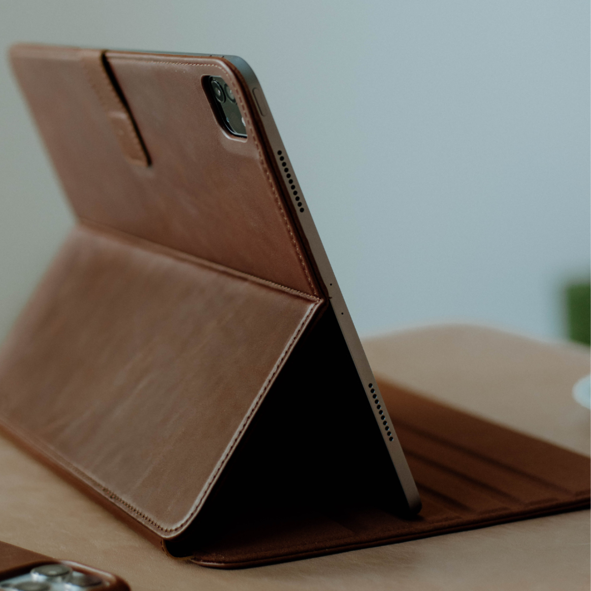 Tablet in a brown leather folio case propped open in landscape, showing the rear camera and side speaker grilles.