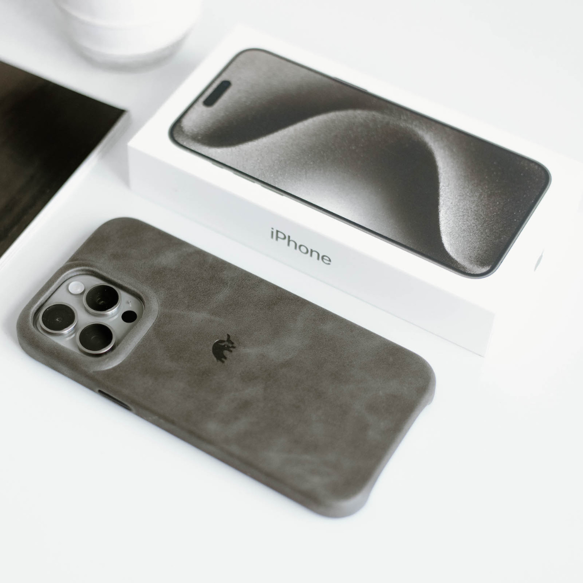 Slate leather Minimalist Case on an iPhone with triple-camera module, resting beside an iPhone box