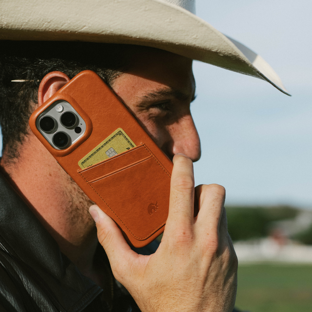Person holding phone to ear wearing sienna leather wallet case with two-card slot showing a gold card