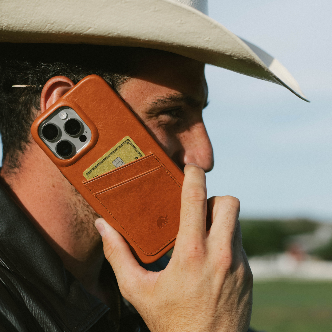 Person holding phone to ear wearing sienna leather wallet case with two-card slot showing a gold card