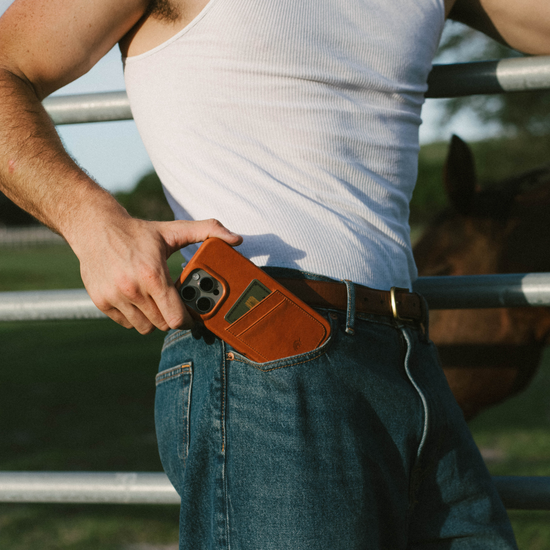 Person sliding phone into sienna leather minimalist portfolio case with visible card pocket at jeans waistband