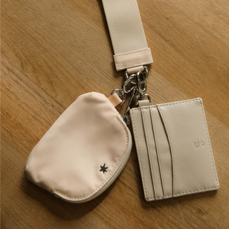 Overhead view of The Carrie Trackable Wristlet in buttercream with matching cardholder showing card slots and metal clasp on a wooden surface