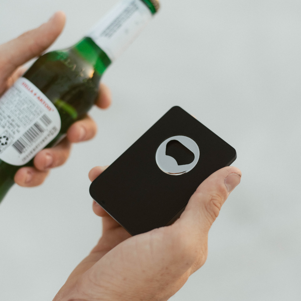 A person holding the Magnetic Popper Wallet, showcasing its built-in bottle opener, with a beer bottle in the other hand.