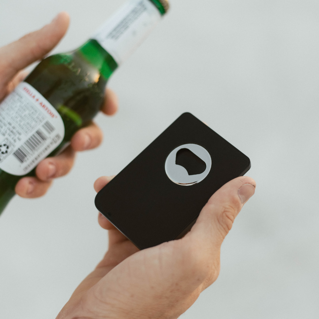 A person holding the Magnetic Popper Wallet, showcasing its built-in bottle opener, with a beer bottle in the other hand.