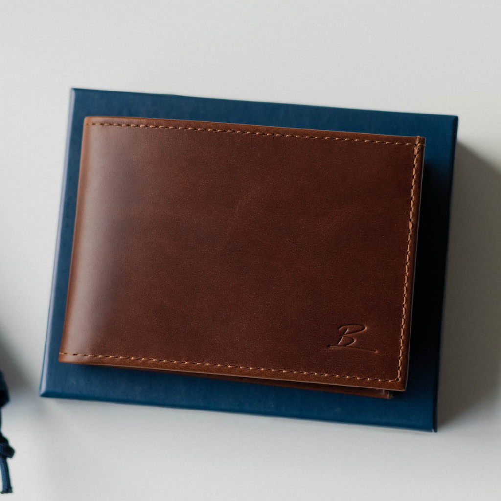 Brown leather bifold wallet on a blue box, embossed with 'B' logo