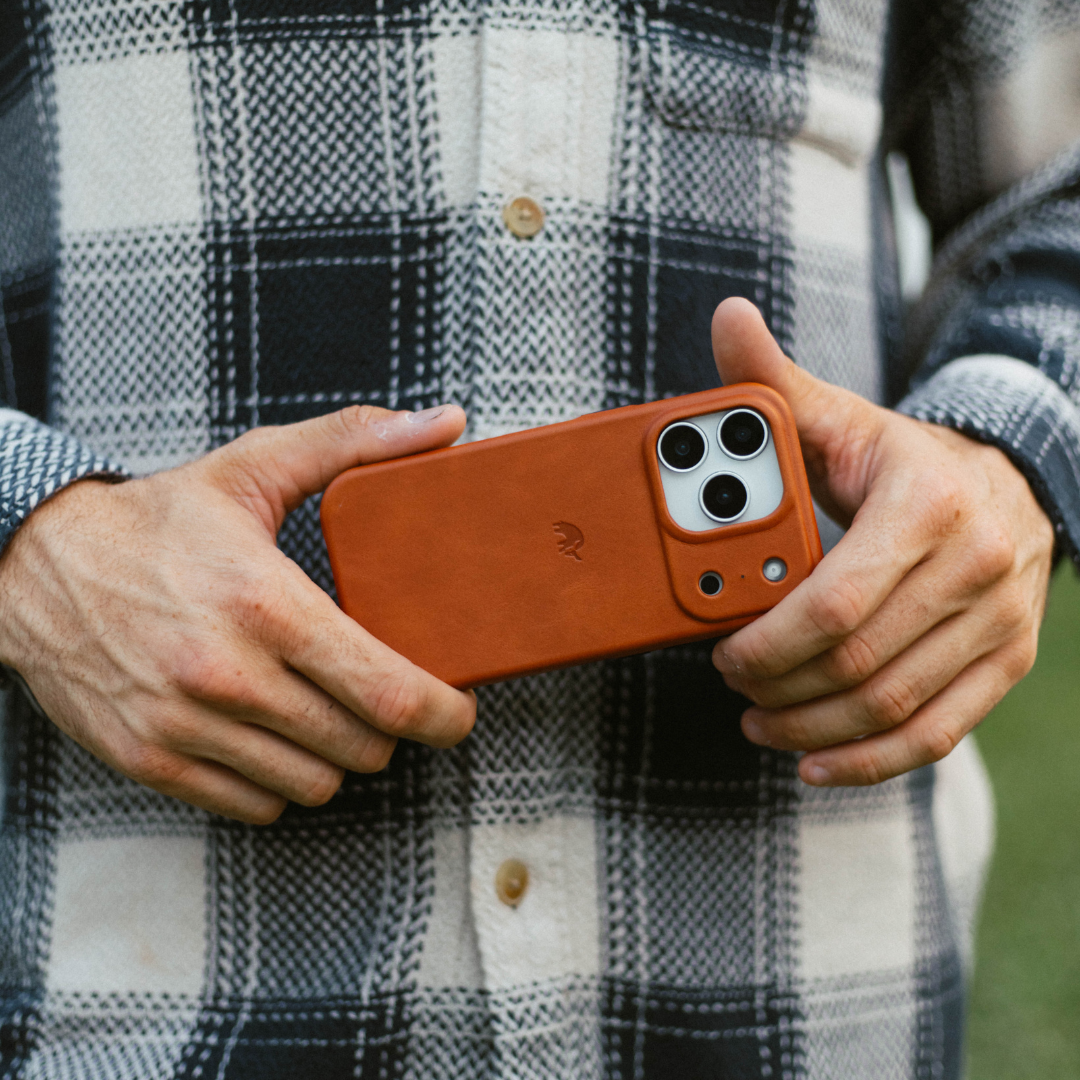Sienna leather phone case on iPhone held in hands, shown against a black-and-white plaid shirt