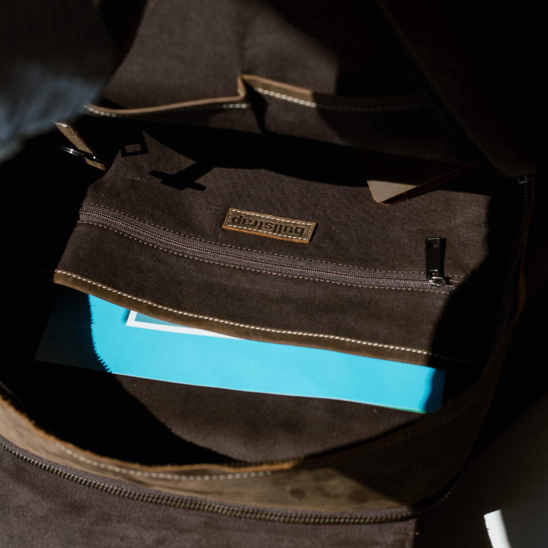 Open brown leather backpack showing interior pocket with "bullstrap" label and a blue notebook.