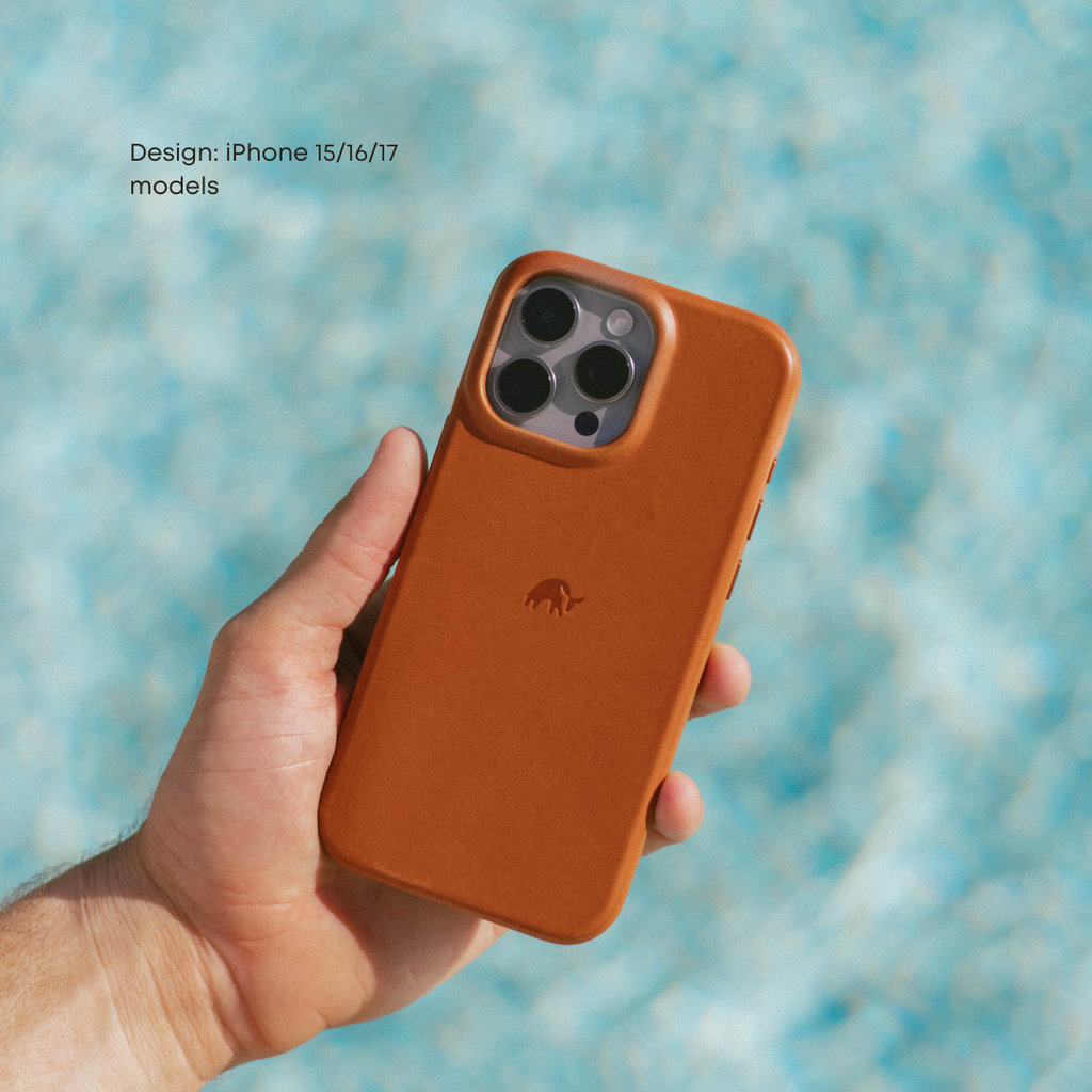 Hand holding The Flex Case in Sienna, back view showing camera cutout, embossed logo and leather finish against blue background.