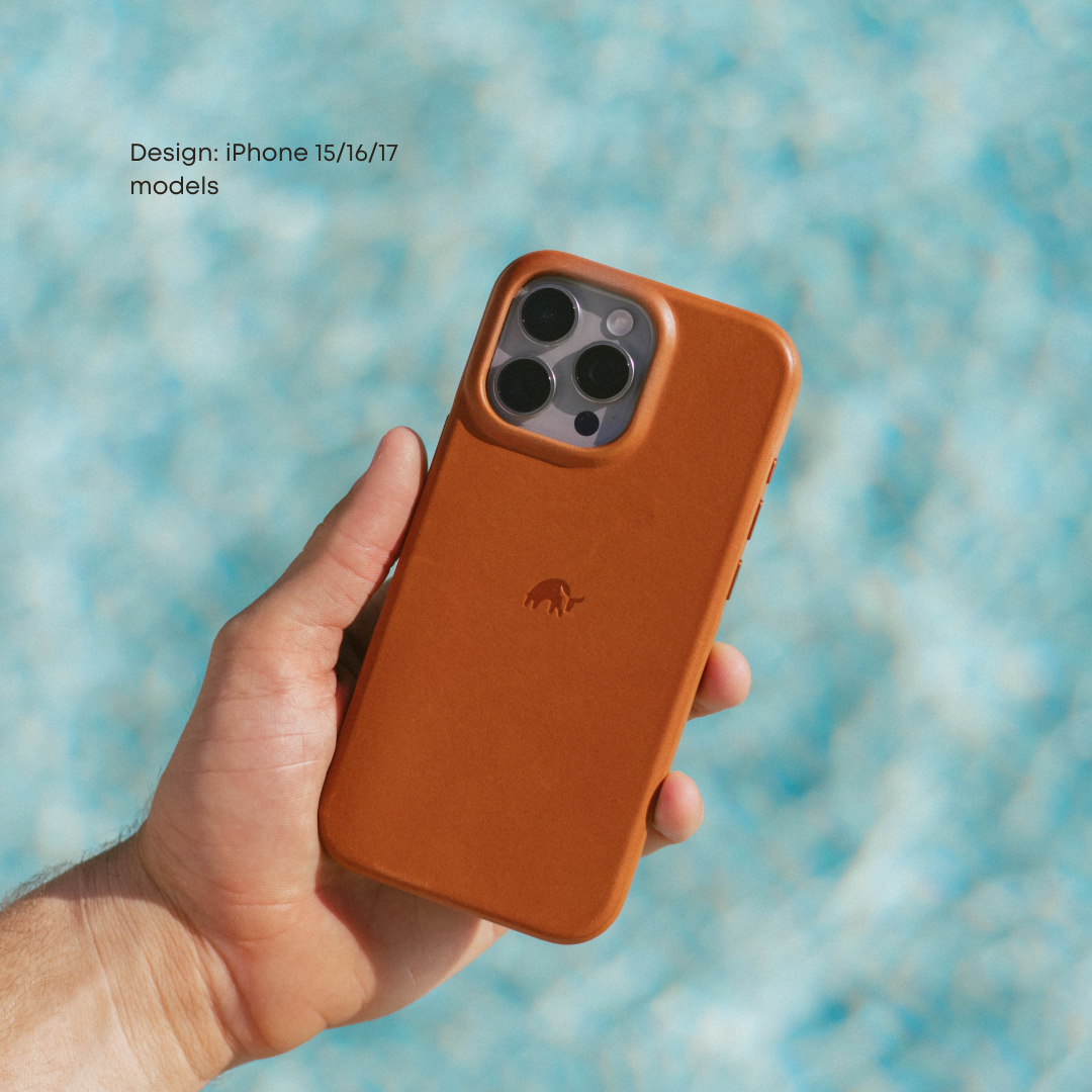 Hand holding The Flex Case in Sienna, back view showing camera cutout, embossed logo and leather finish against blue background.
