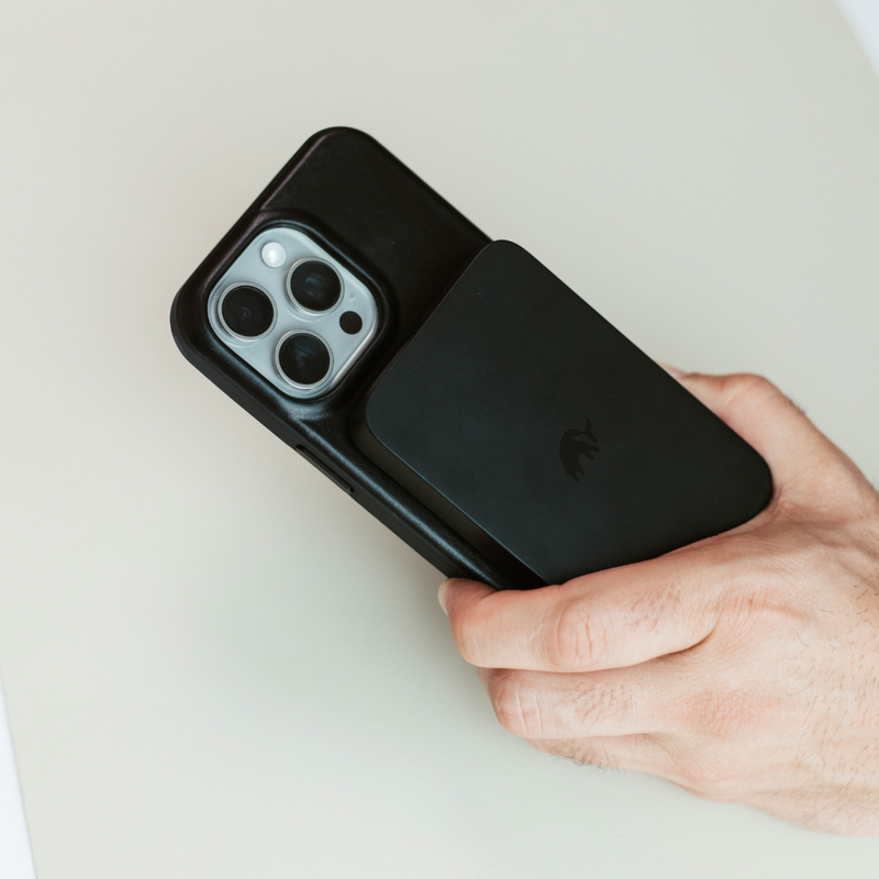 A hand holding the MagSafe Power Bank attached to an iPhone.