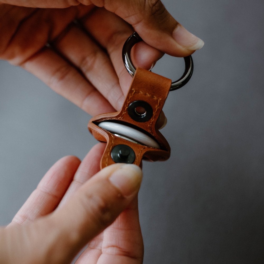A person holding a BullTag for AirTag in sienna leather with a stainless-steel clip.