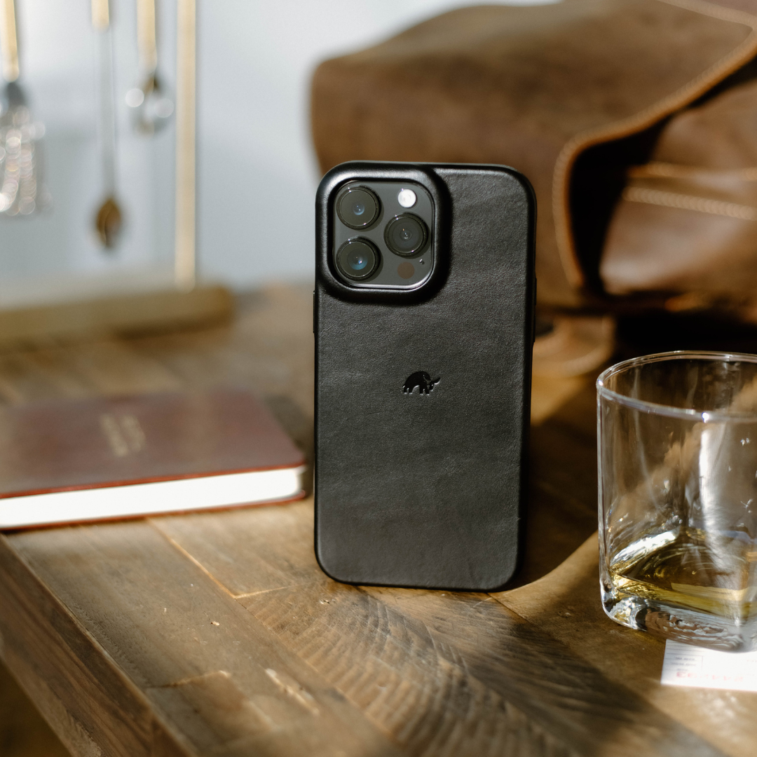 Black leather phone case standing upright on wooden table, next to a glass and notebook
