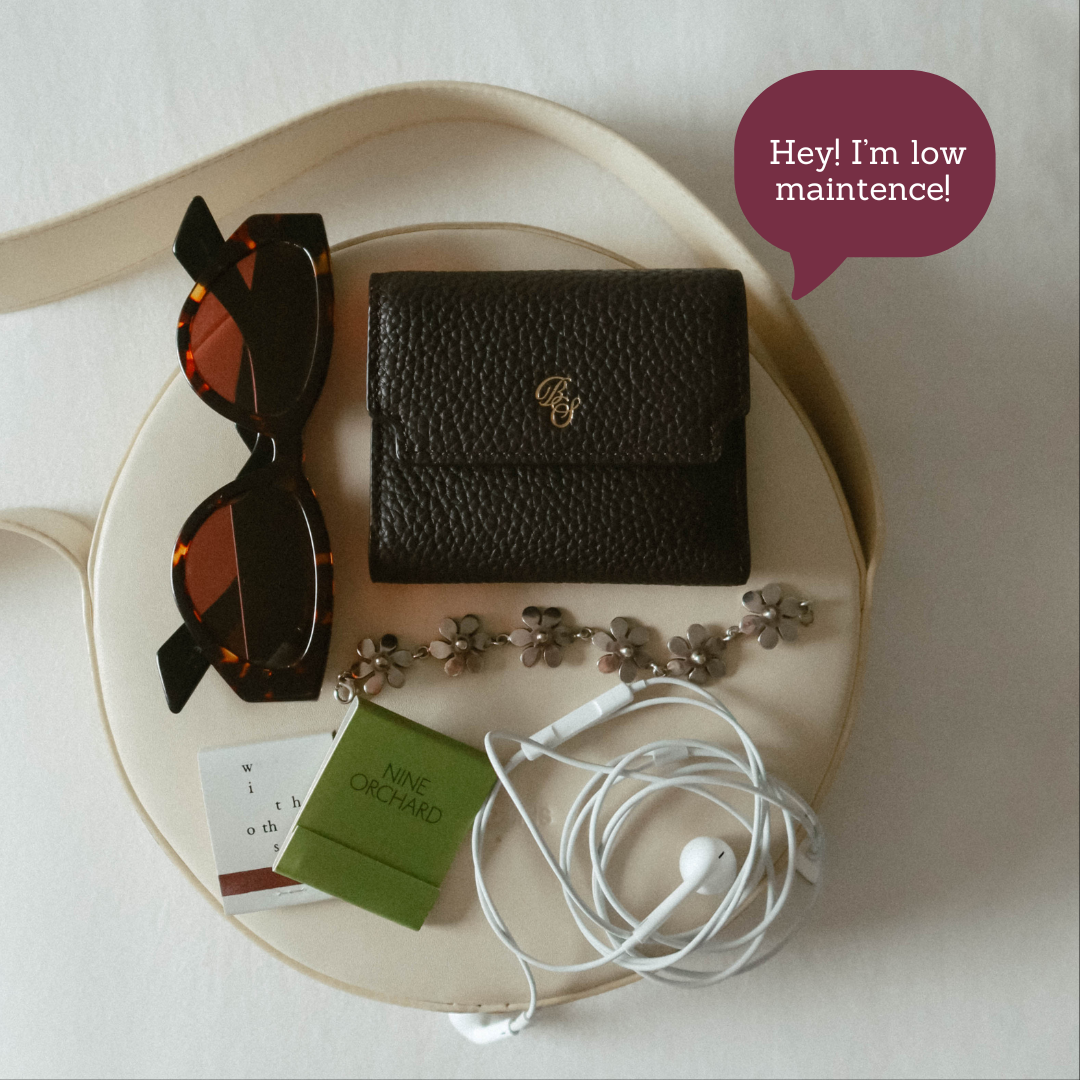 Pebbled trifold wallet with sunglasses, earbuds and green NINE ORCHARD box; speech bubble reads: Hey! I'm low maintence!