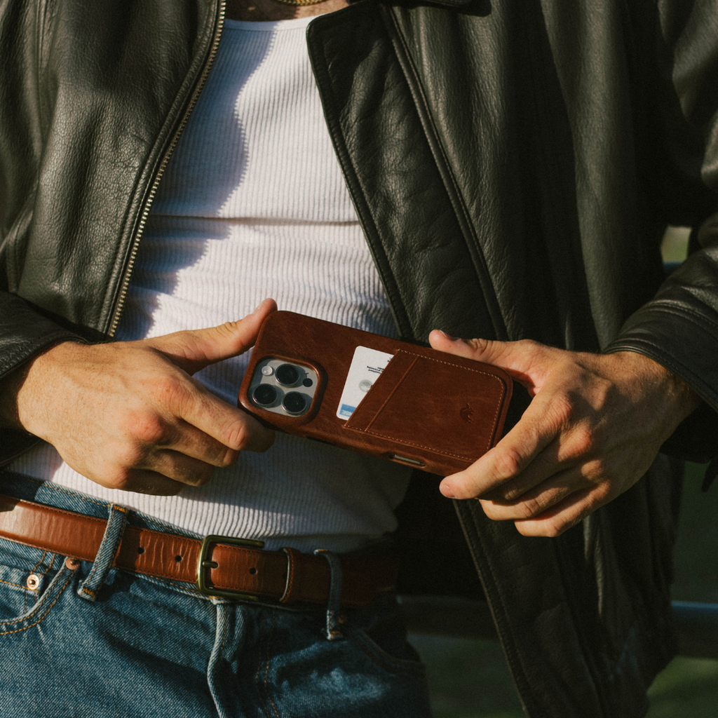 Hands holding brown leather wallet-style iPhone case with a visible card in the rear card slot.