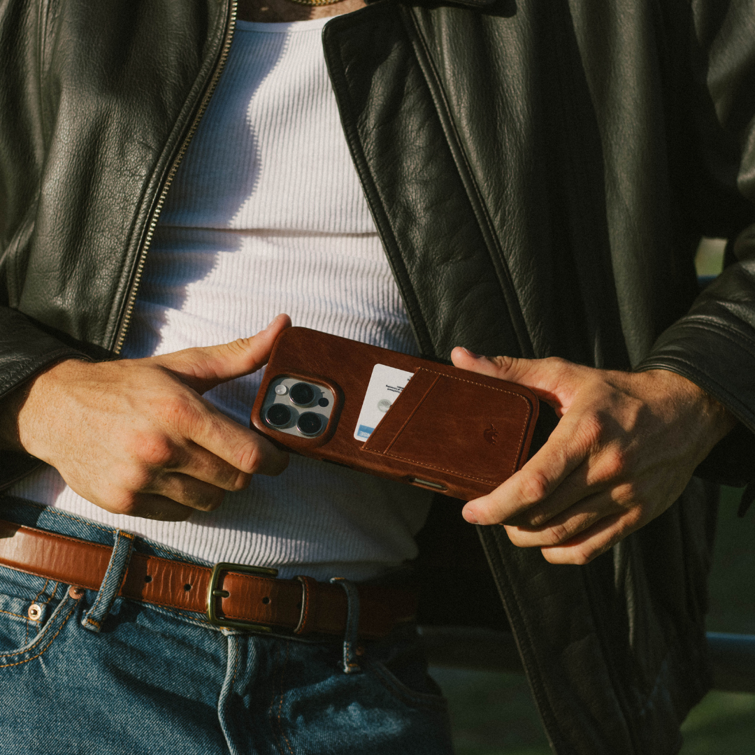 Hands holding brown leather wallet-style iPhone case with a visible card in the rear card slot.