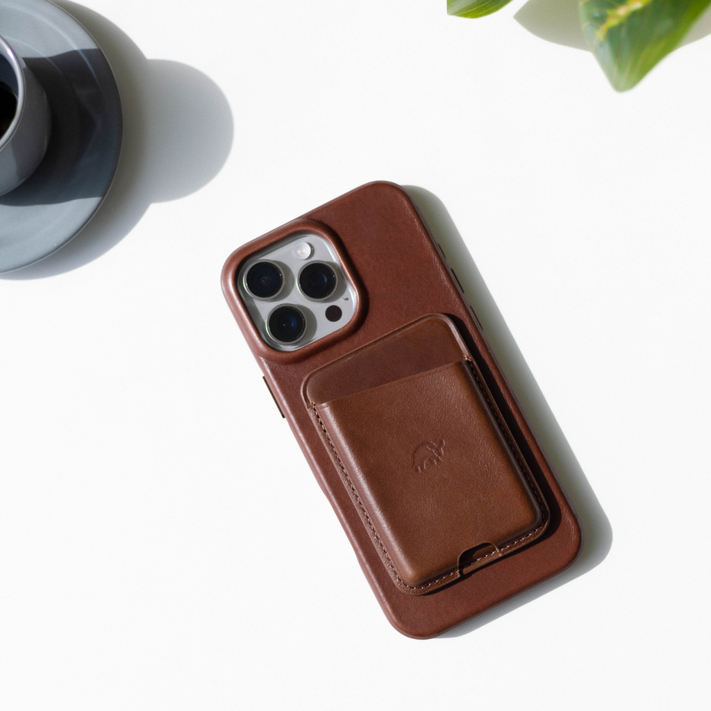 The Flex Case in Terra color, featuring a card holder, on a white surface with a plant and cup in the background.