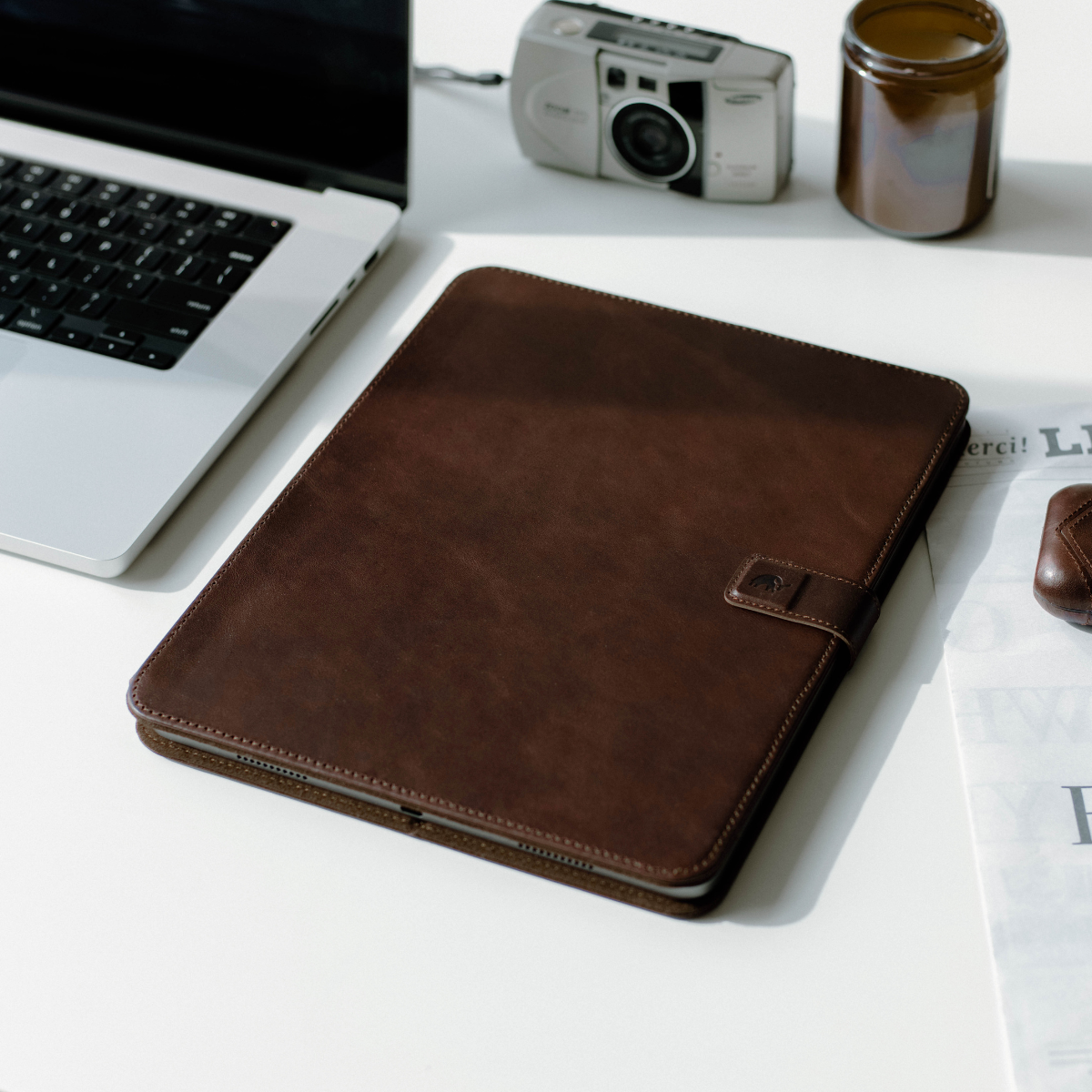 Brown leather iPad case on a desk with a laptop and camera