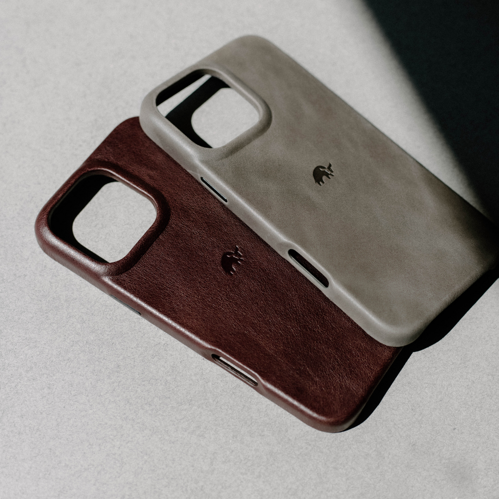 Two leather phone cases overlapping, bourbon brown and light gray, embossed elephant logo