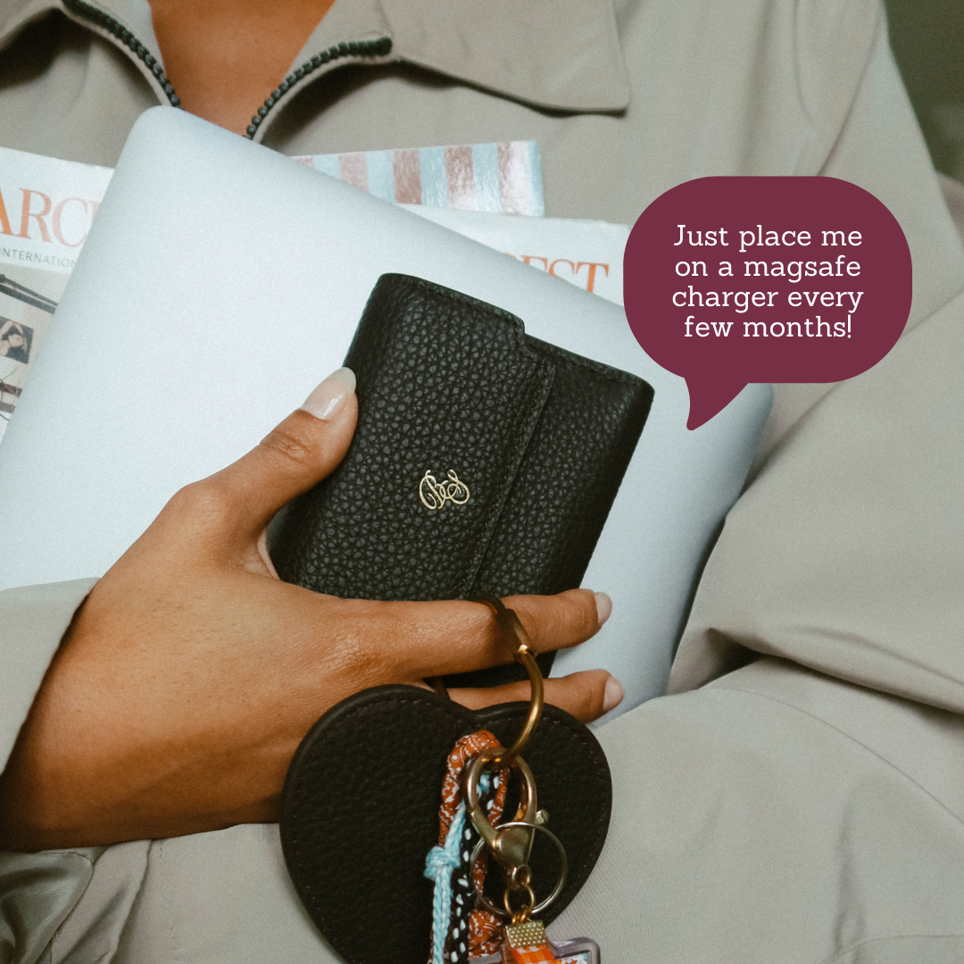Black trifold wallet with heart keyring held in hand; speech bubble: "Just place me on a magsafe charger every few months!"
