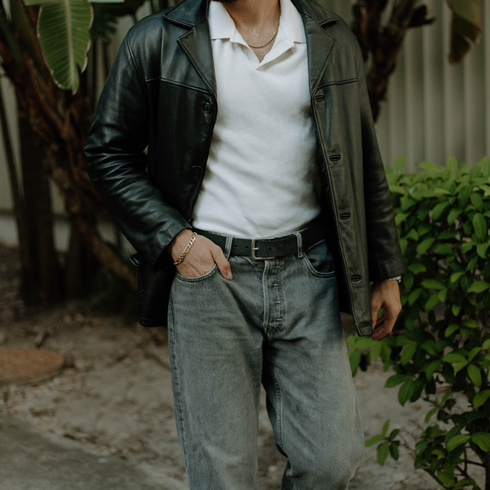 Person wearing a leather jacket and jeans in an outdoor setting showcasing a rugged leather belt in black