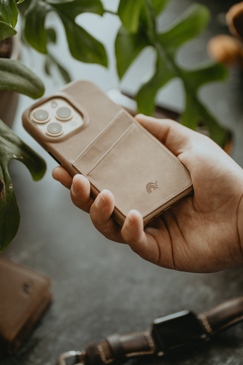 A hand holding a beige leather phone case with card slots.