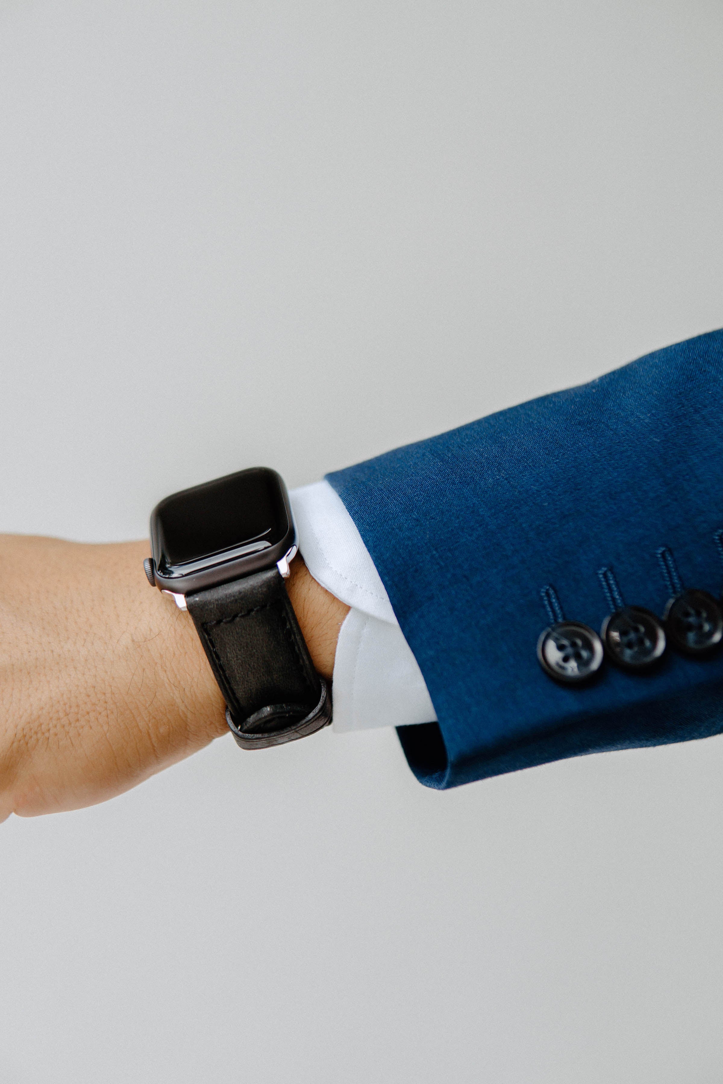 Close-up of a wrist wearing a smartwatch with a black leather strap, dressed in a blue suit.