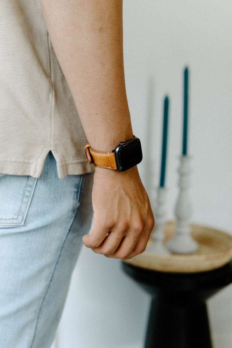 A person wearing a leather Apple Watch strap on their wrist, with a blurred background of a candle holder and a table.