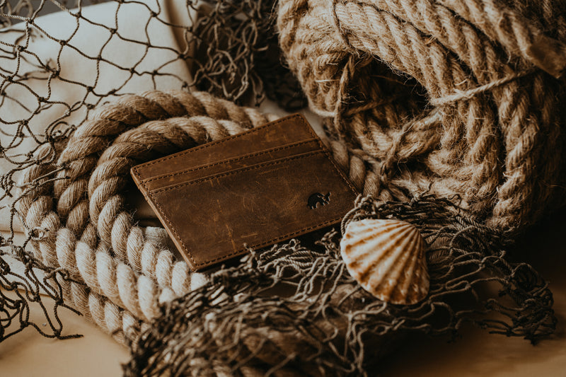 A leather cardholder placed on textured ropes and a shell.