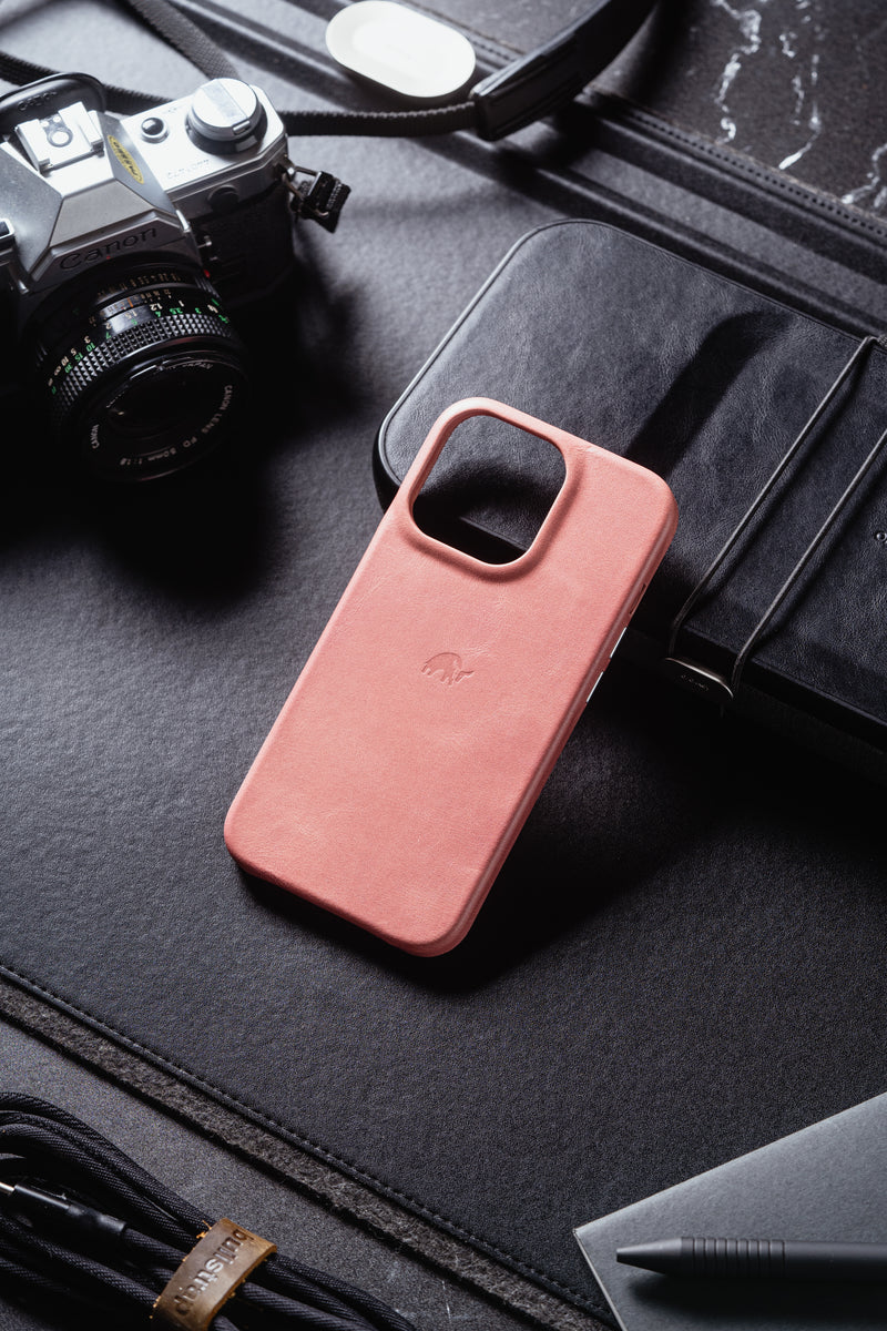 Pink leather smartphone case with large square camera cutout and embossed elephant logo on black desk beside a Canon camera