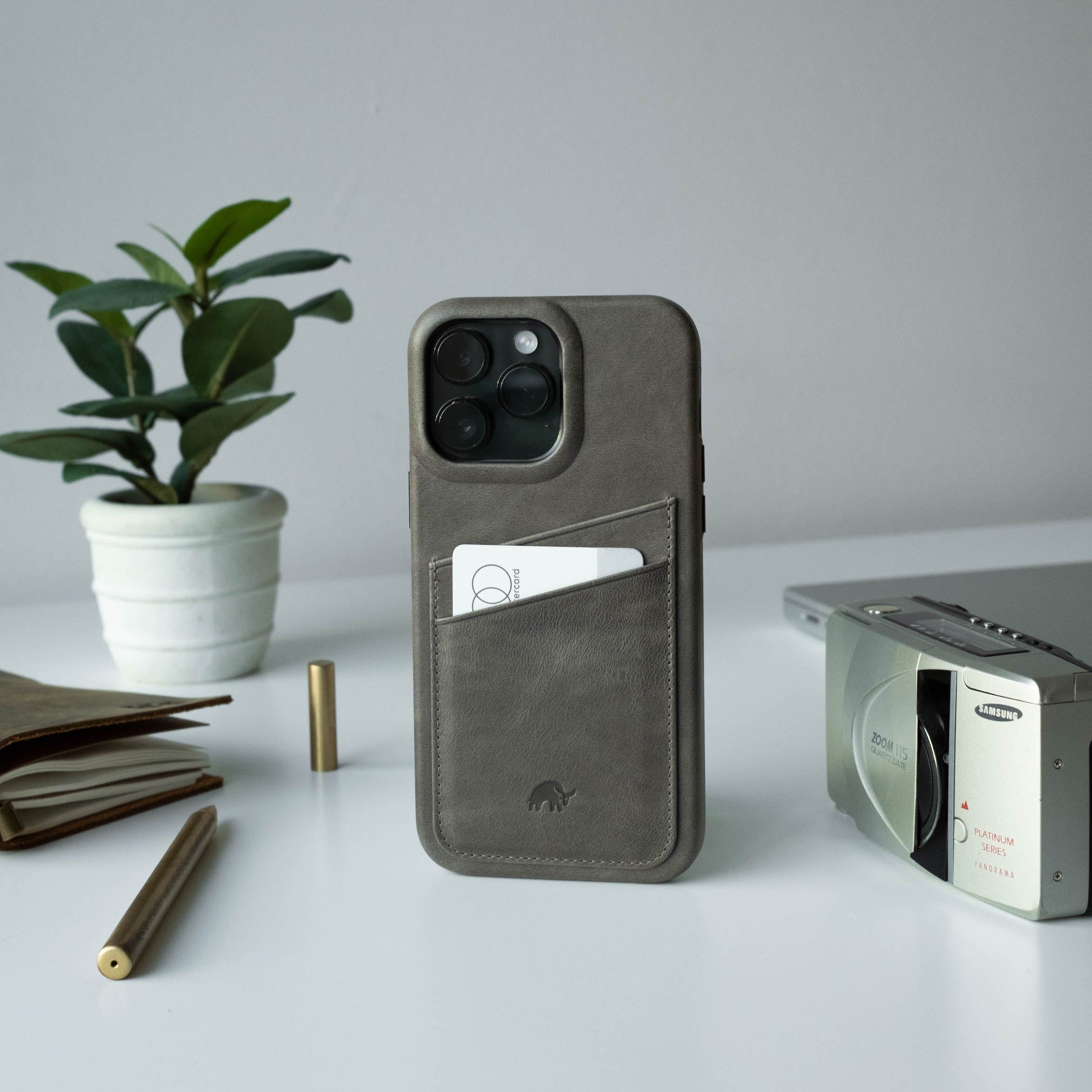The Minimalist Portfolio Case in slate color with a card slot, placed on a desk with a plant and camera