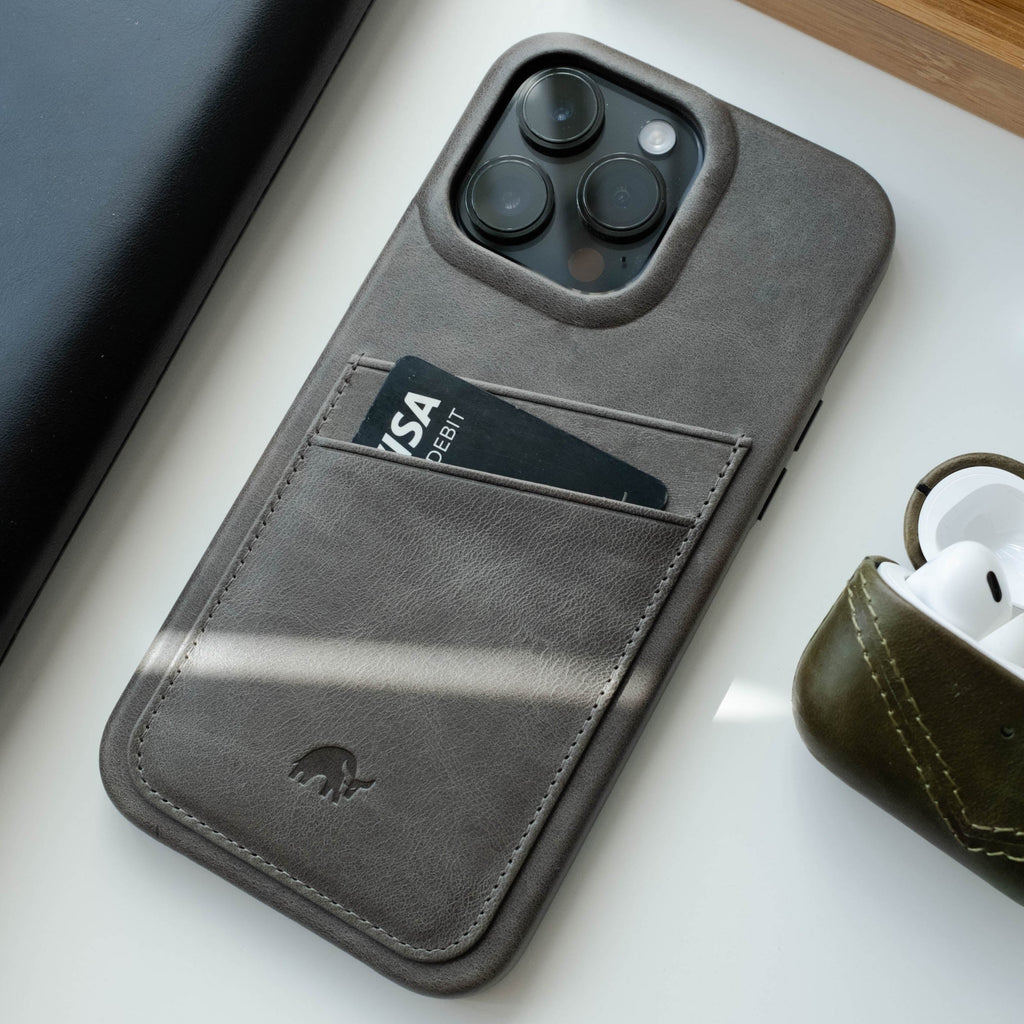 Slate leather phone wallet case holding a VISA DEBIT card, photographed beside AirPods on a white surface.