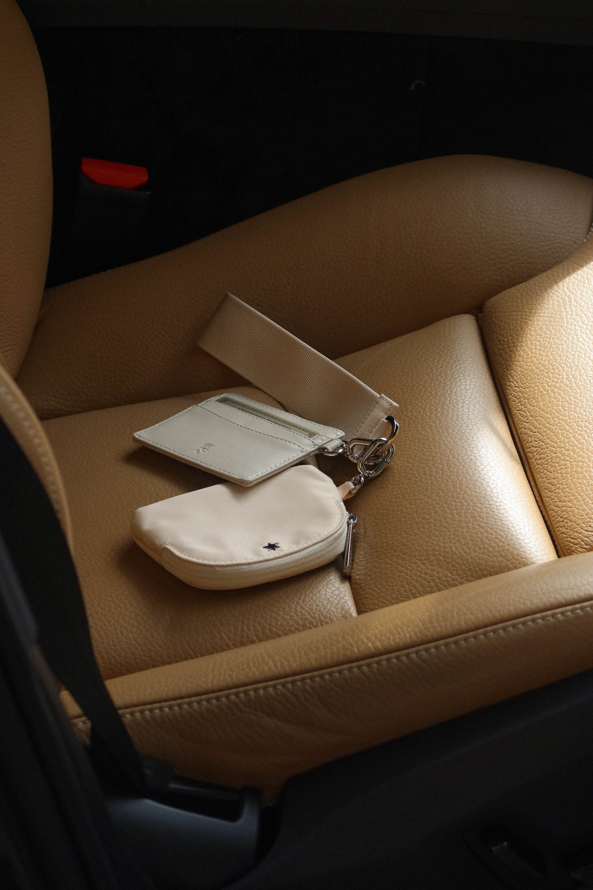 Small beige cardholder and zip pouch attached to a strap resting on tan leather car seat