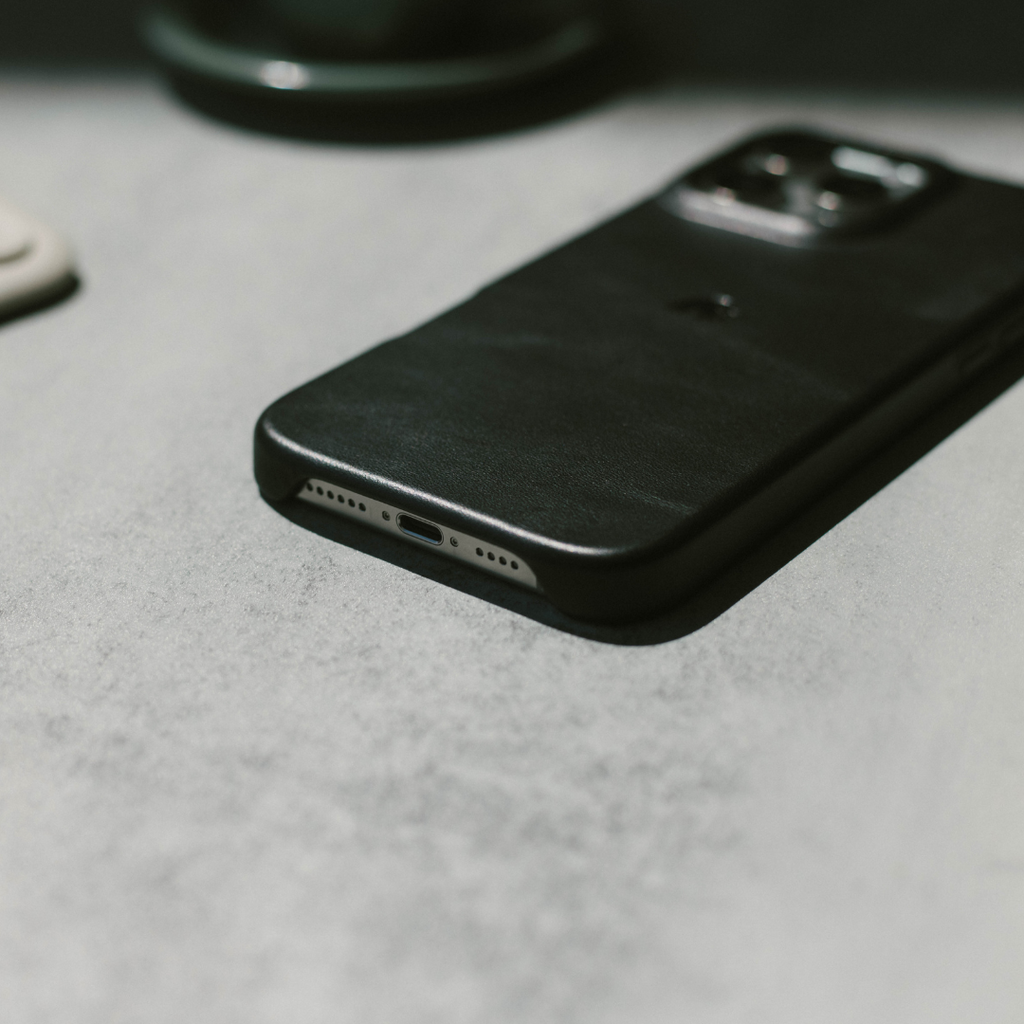 Slim black phone case on a gray tabletop, angled view showing back and bottom charging port cutout