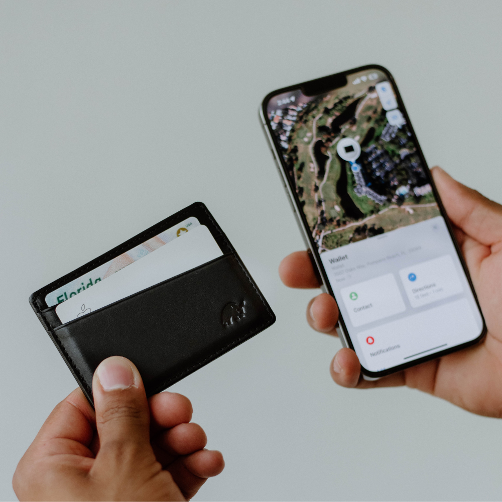A person holding a leather wallet with cards next to a smartphone displaying a map.
