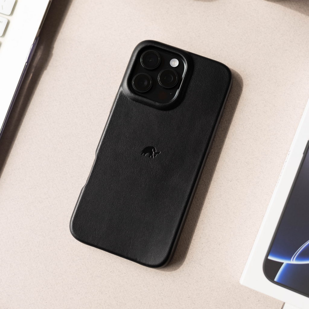 Black leather phone case with raised camera lip and embossed bull logo, shown on beige surface