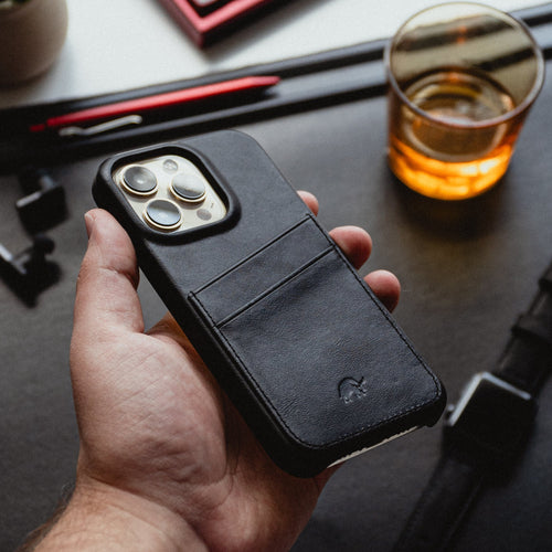 A person holding the Minimalist Portfolio Case in black with card slots, set on a desk with a drink and stationery.