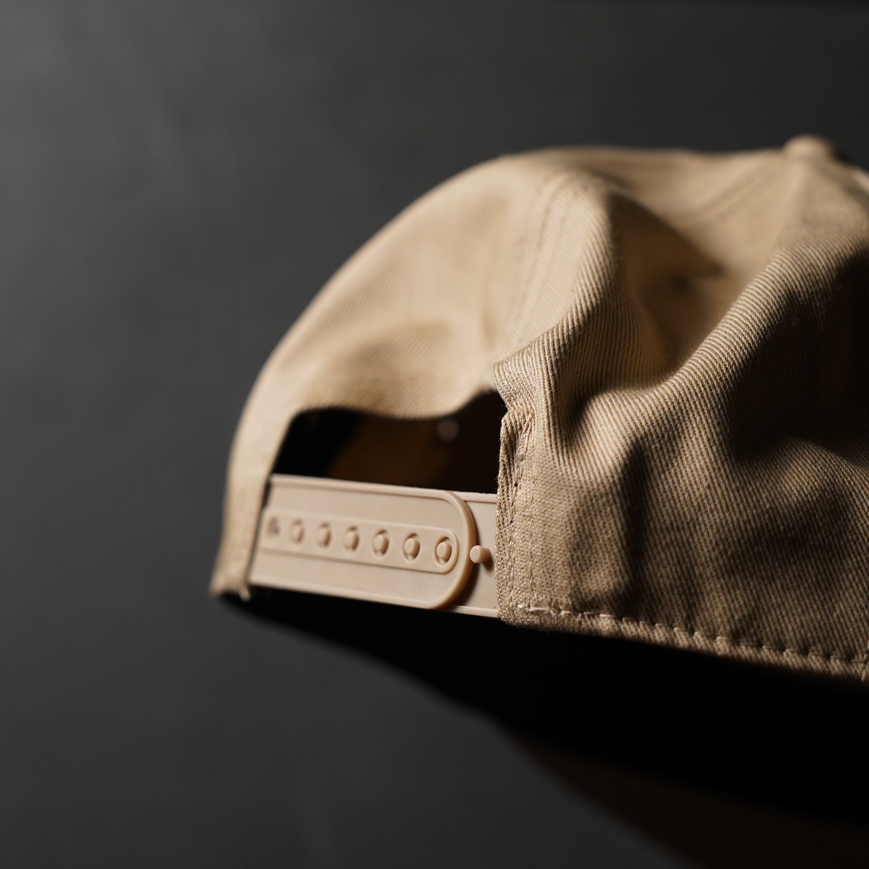 Close-up of the back of a tan hat showing the snap-back adjustment.