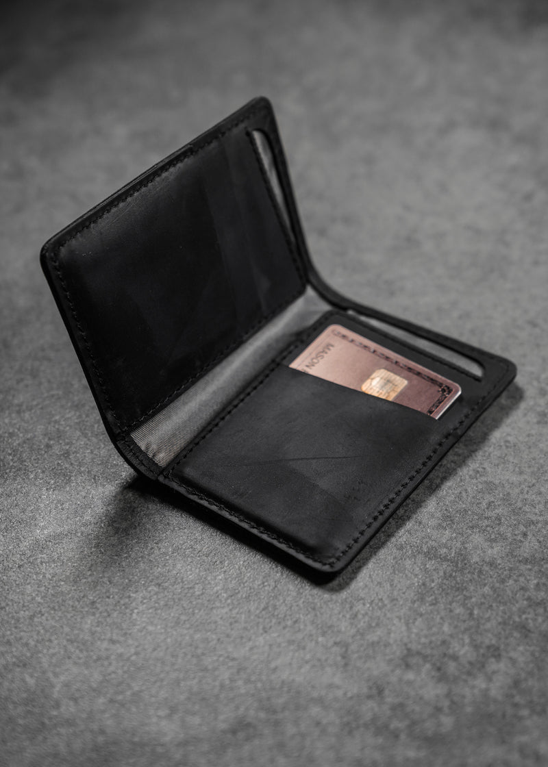 Open black leather wallet on gray surface with a partially visible copper card showing an EMV chip.