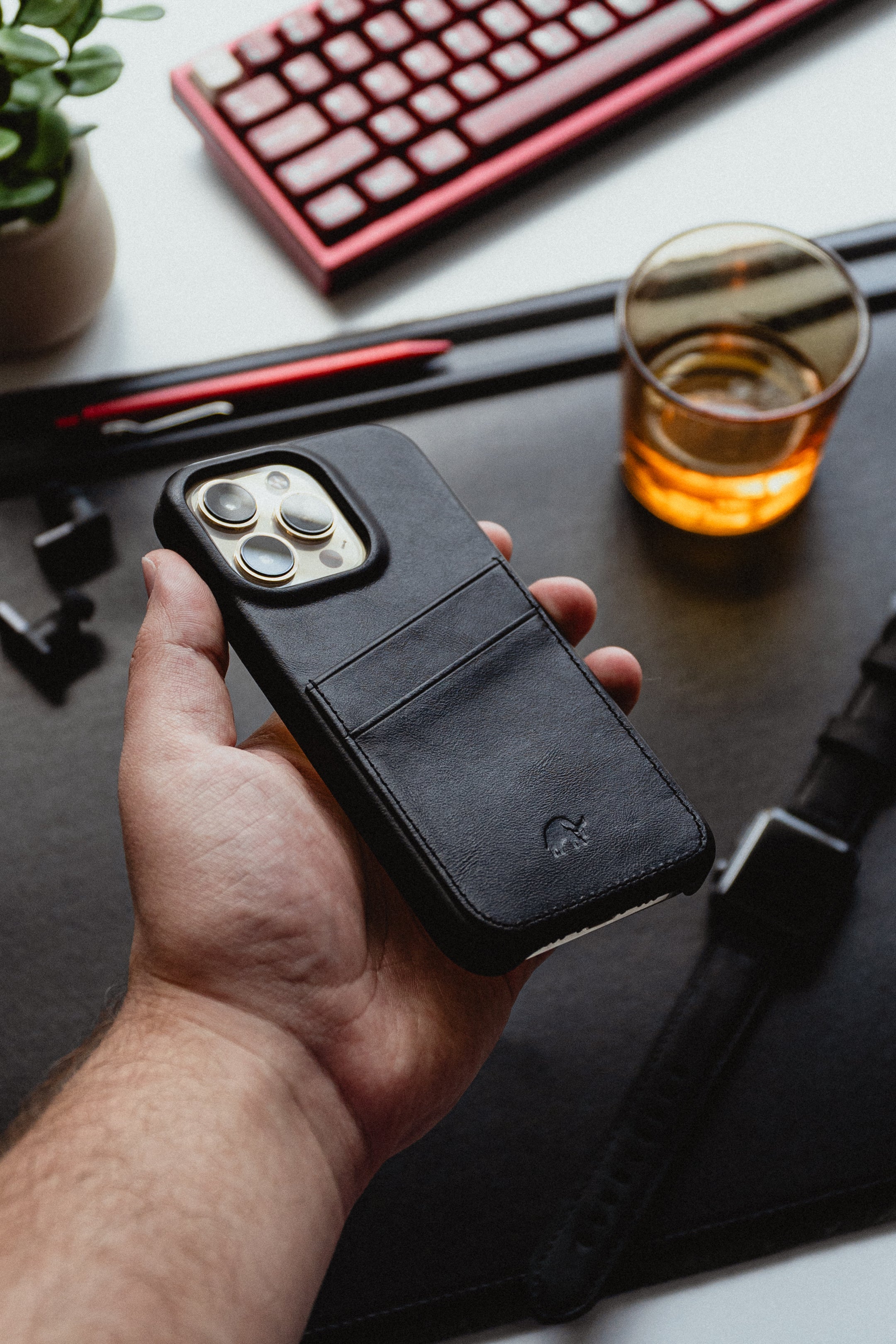 A hand holding a black leather iPhone case with card slots.