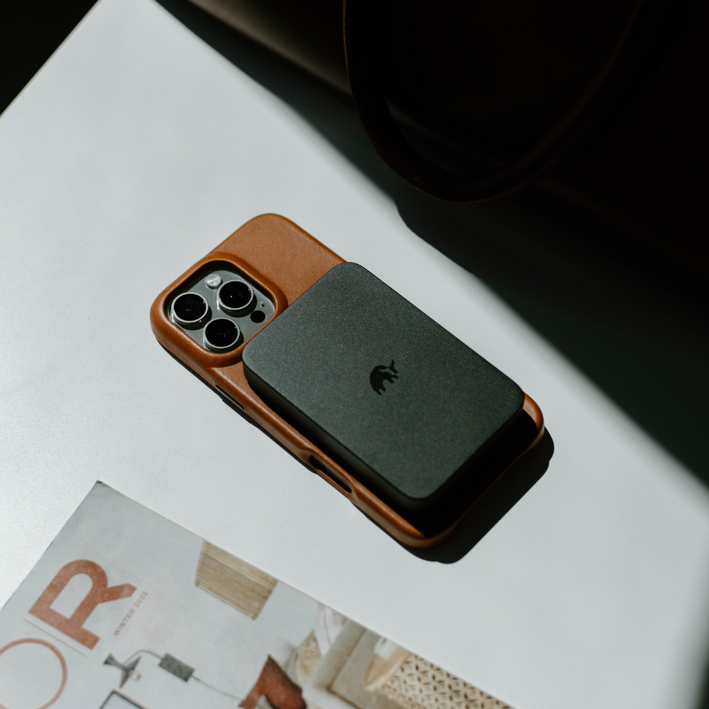 A MagSafe Power Bank attached to an iPhone on a table with a magazine underneath.
