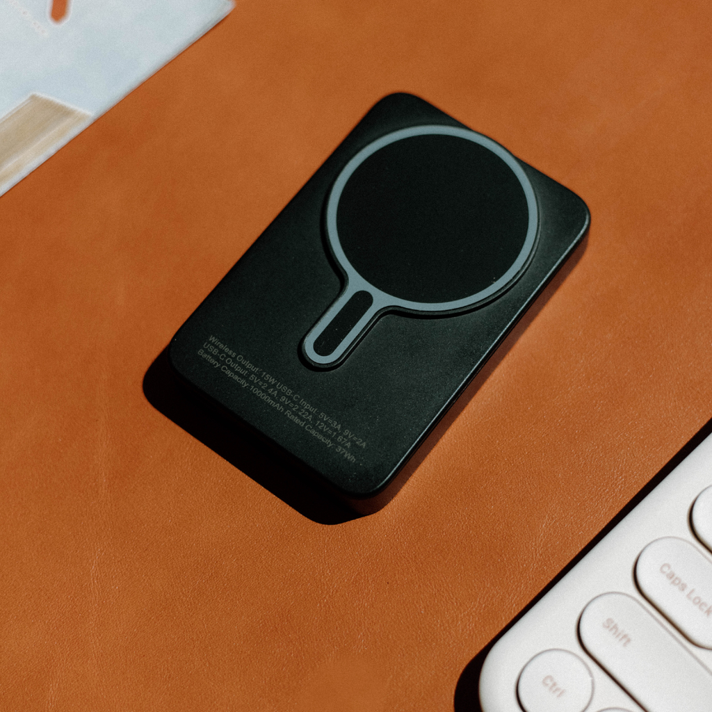 Bullstrap MagSafe power bank with circular charging pad on tan leather, beside keyboard keys labeled 'Caps Lock', 'Shift', 'Ctrl'.
