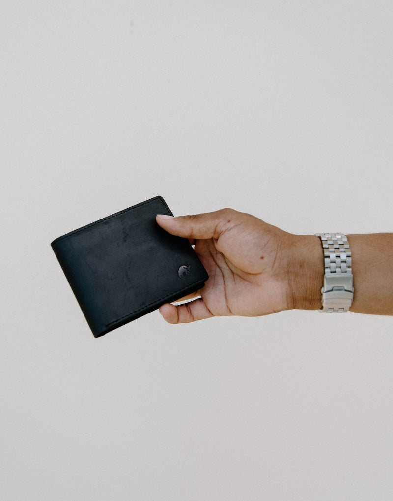 A hand holding a black bifold wallet with a silver watch on the wrist.