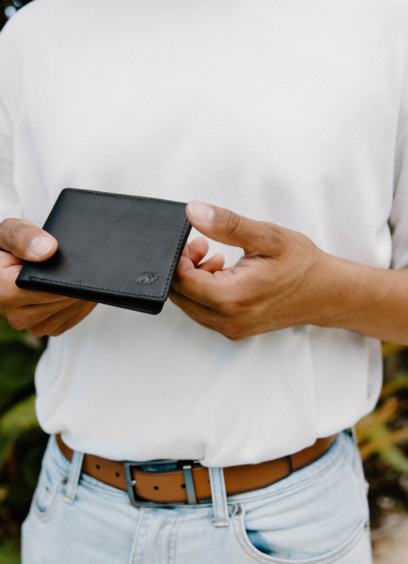 Black leather bifold wallet held in both hands, embossed elephant logo on lower corner.