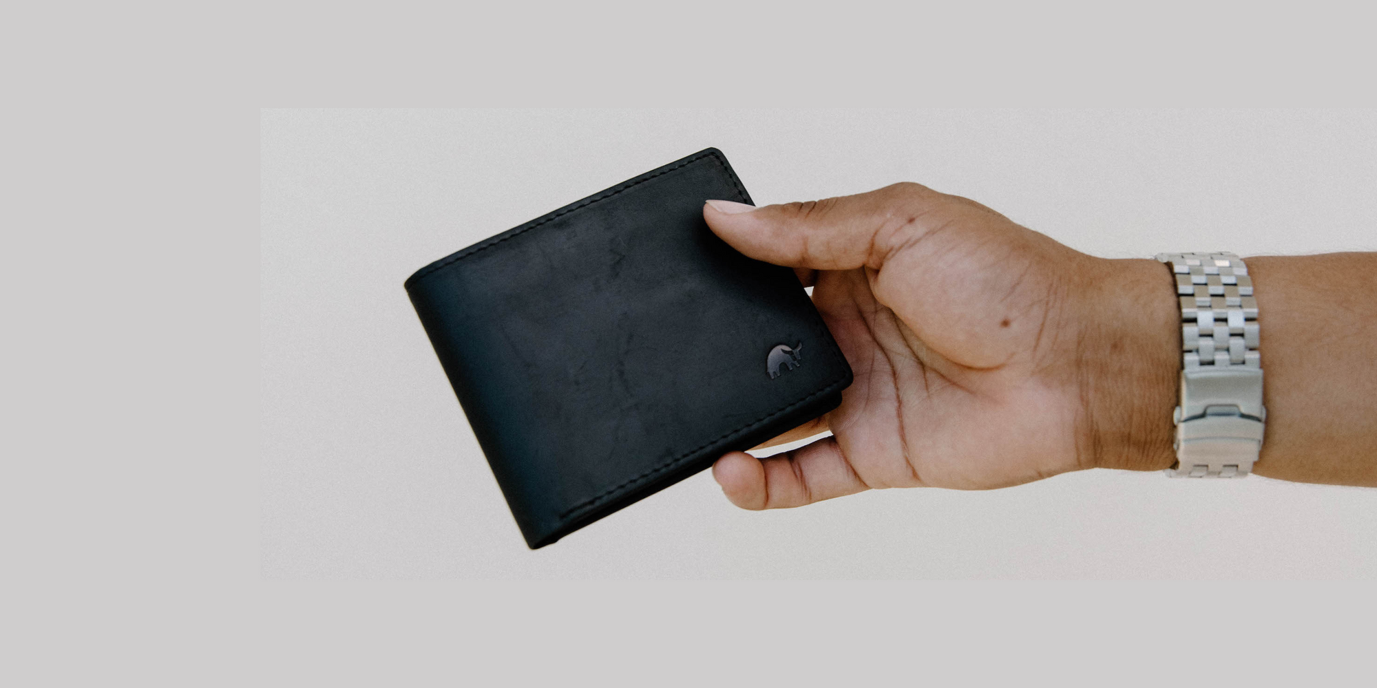 Hand holding a black bifold wallet with a small elephant logo; wrist with a silver metal watch visible